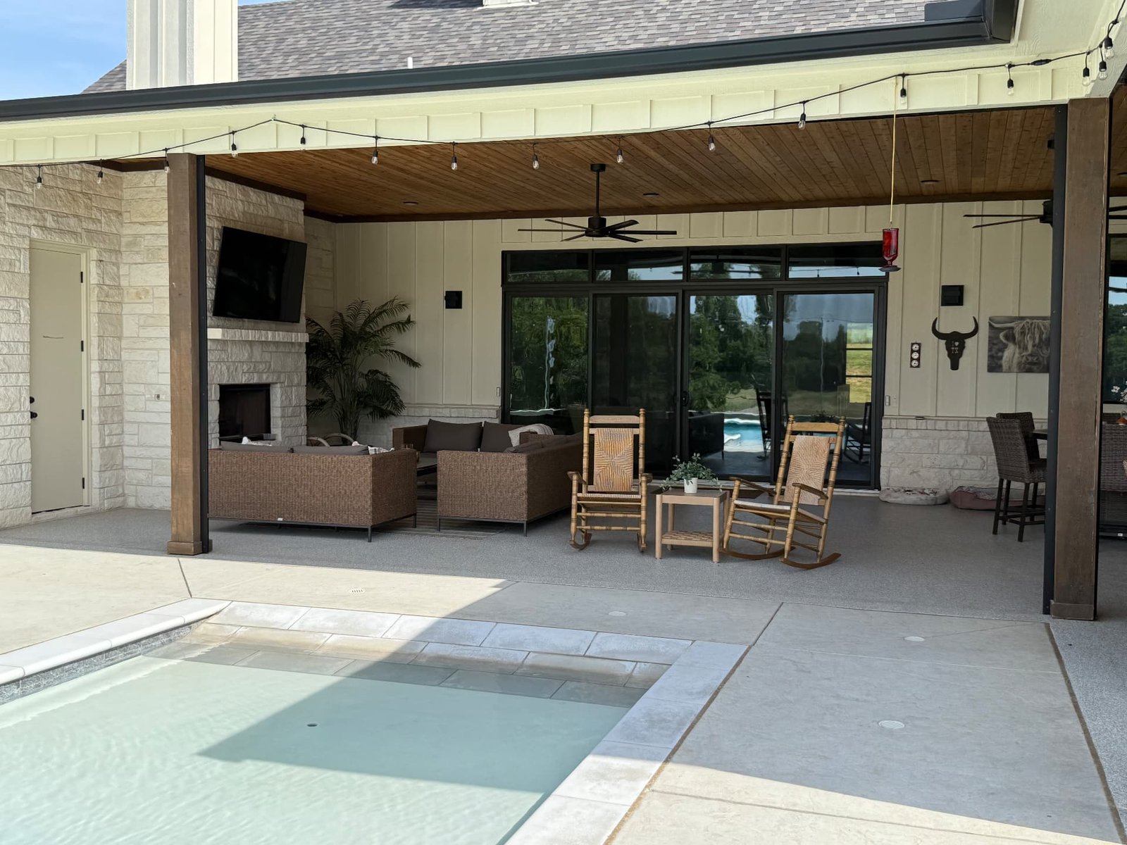 Motorized retractable patio screens on a covered Texas patio with comfortable seating, fireplace and pool.